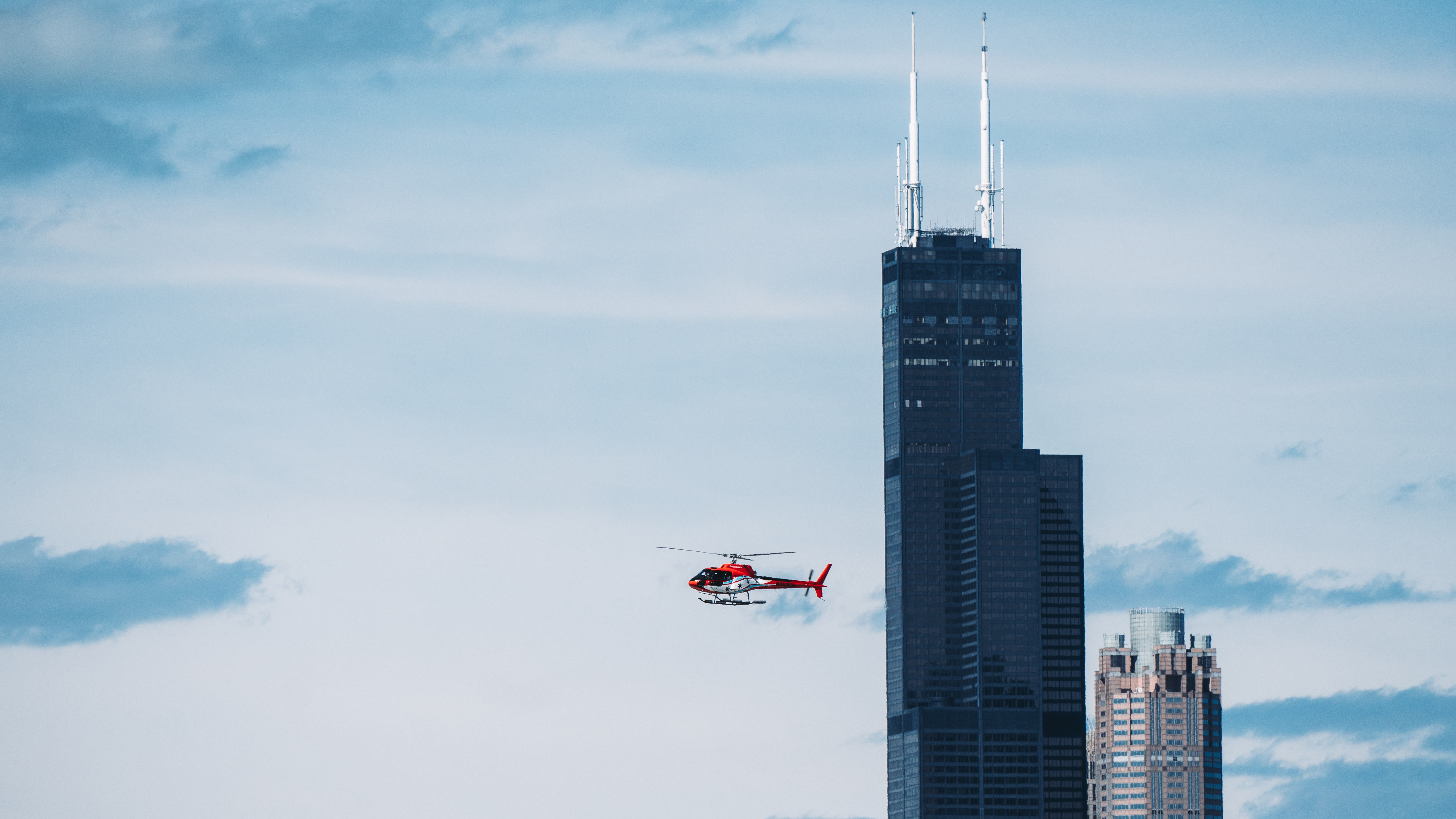 Red helicopter flying towards the left, away from a black skyscraper.